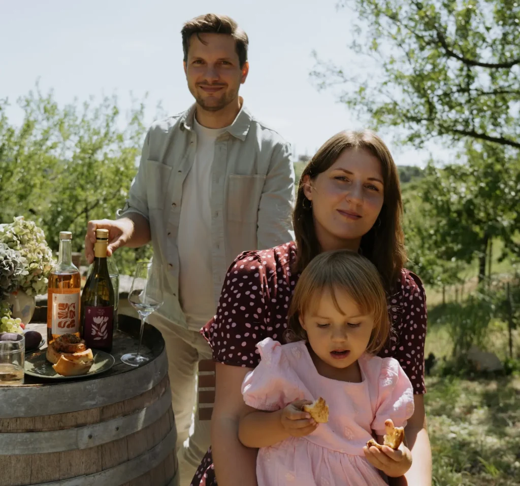 Familie genießt lokale Weine und Snacks in einem Weinberg, umgeben von grünen Reben und sonnigem Wetter.