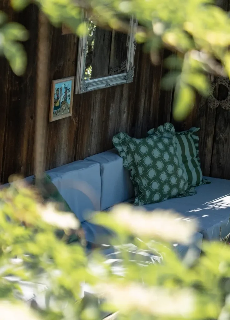 Gemütliche Sitzecke mit grünen Kissen und Holzverkleidung, umgeben von Pflanzen und einem Spiegel an der Wand.